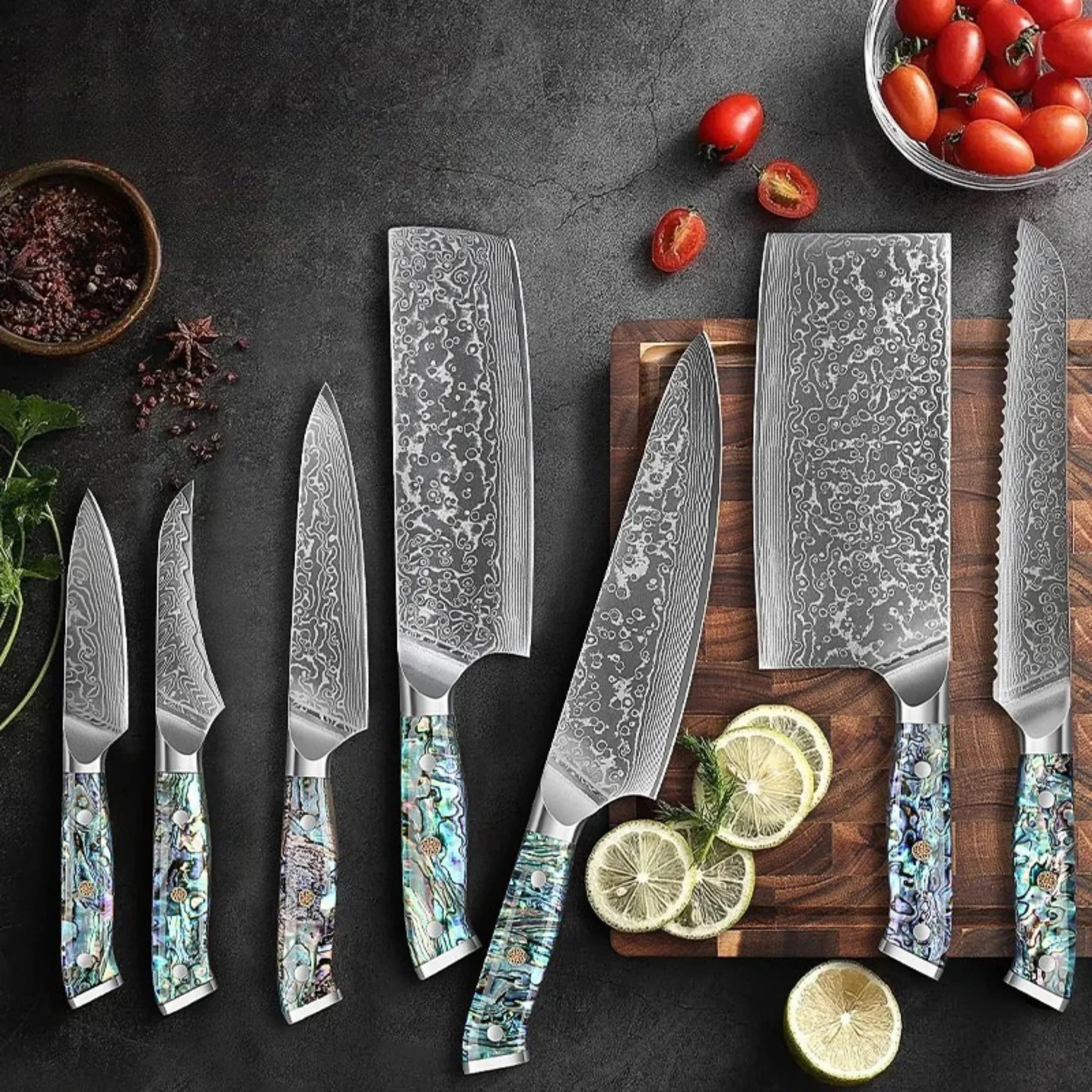 Damascus steel kitchen knife set with abalone-style handles on dark counter, cutting board and fresh vegetables.