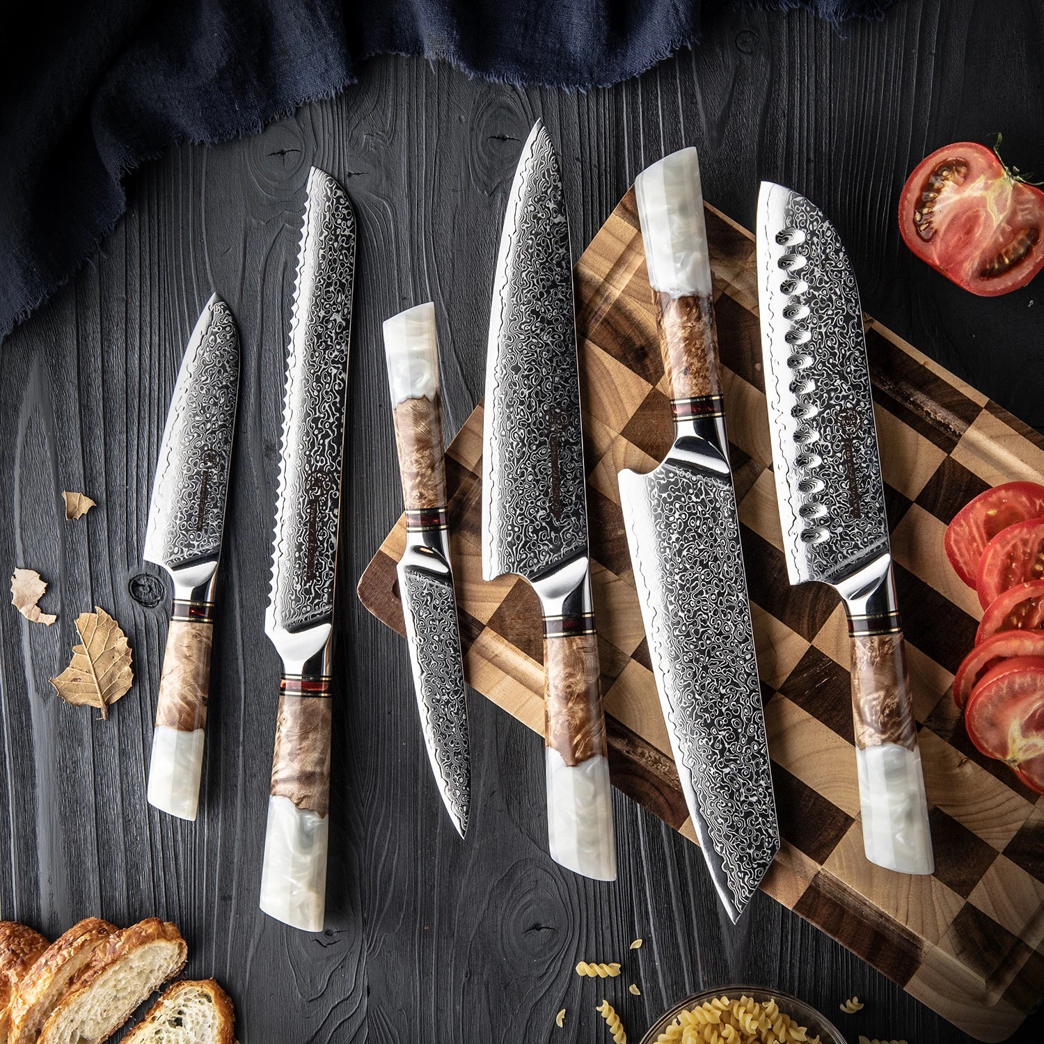 Set of Damascus steel kitchen knives with wood and pearl handles on a cutting board