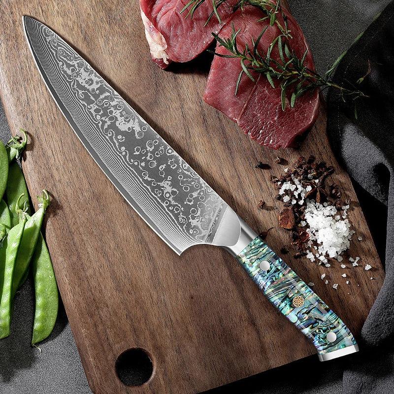 Damascus steel chef knife with abalone handle on cutting board with beef, salt, and spices